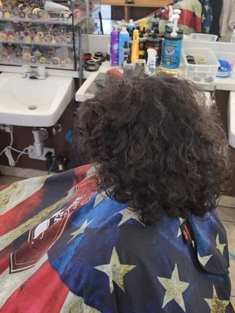 Client with long curly hair in the chair under a stars-and-stripes cape